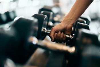 A person's hand is holding a dumbbell in a gym.